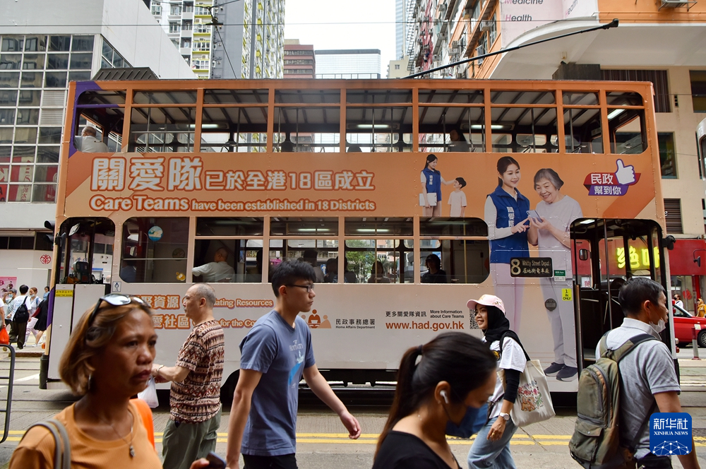 一輛塗裝關愛隊宣傳海報的有軌電車從街頭駛過。(新華社)