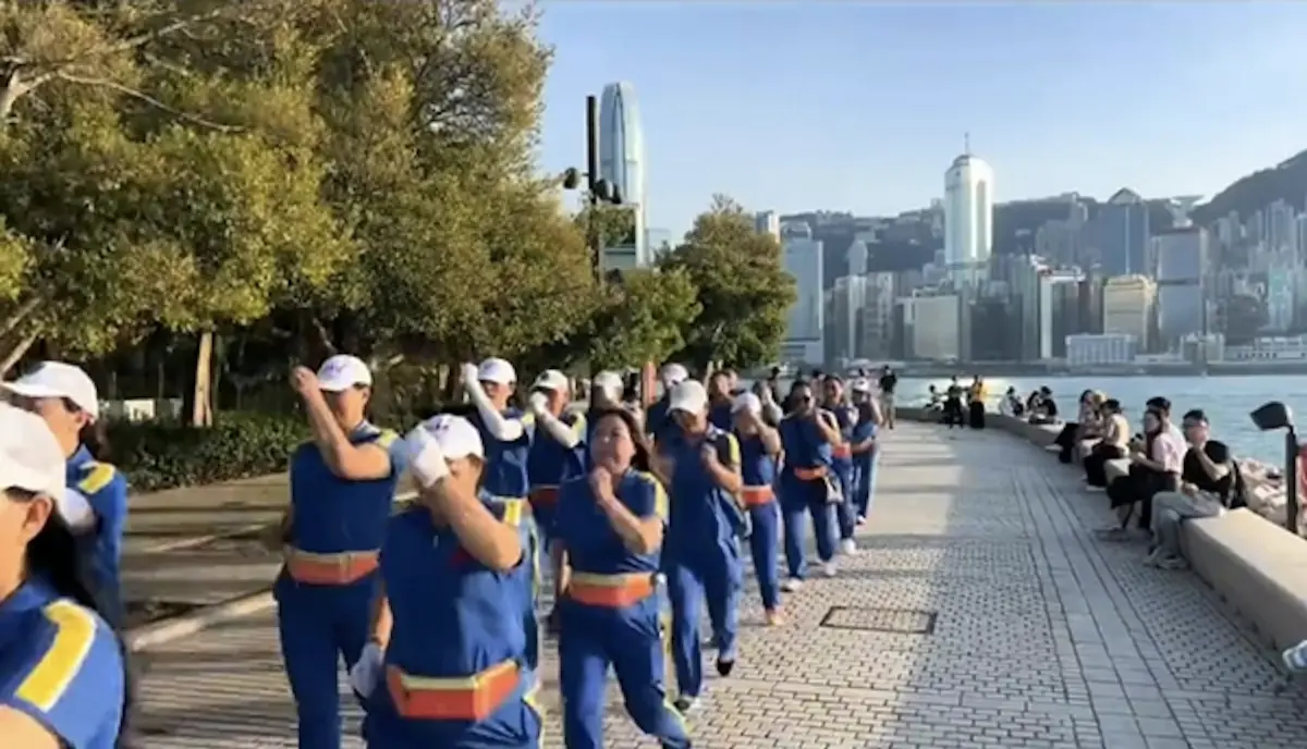 影片畫面顯示，該「暴走團」成員統一穿着藍色團體服，在持旗領隊的帶領下列隊前行，隊伍整齊劃一。行進過程中，團體全程播放音量巨大的音樂助威，部分成員更一邊步行一邊做着伸展運動，獨特的陣容與動作吸引了周圍遊客及本地市民的目光。(圖：視頻截圖)