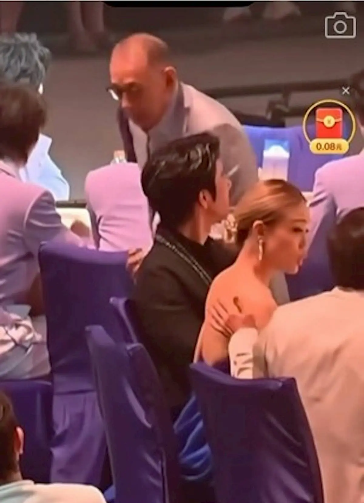 身著大露背深藍晚裝的容祖兒坐在成龍身旁，成龍原本搭在椅背的手輕拍其玉背兩下，隨後掃上膊頭並輕觸肩膀。(圖：視頻翻攝)