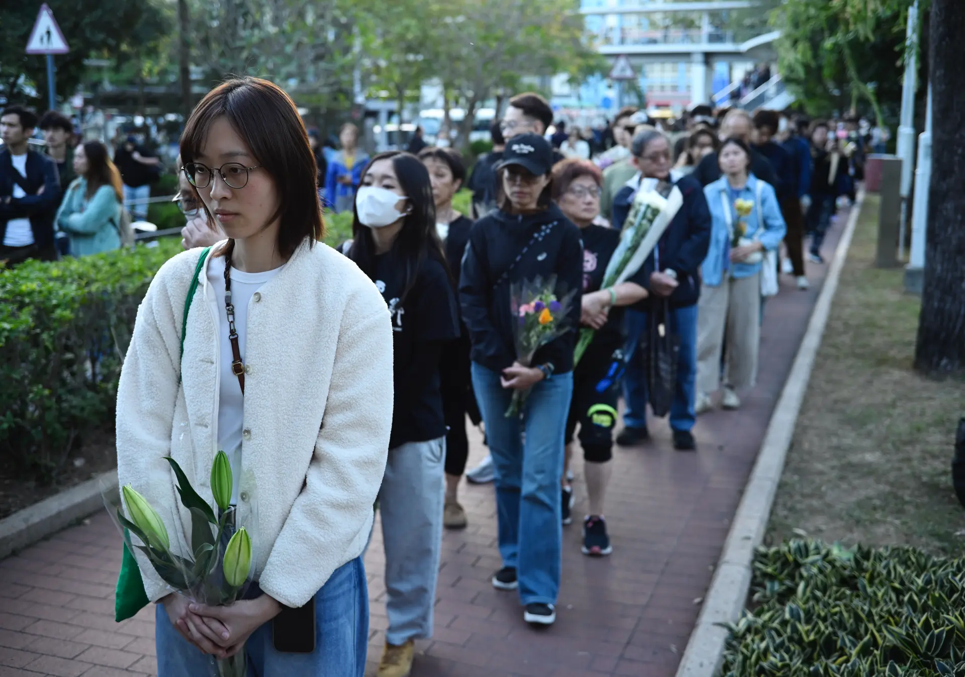 午後的陽光透過樹葉灑在花束上，廣福休憩處的人龍雖長，卻格外安靜。有人輕撫花葉，有人低語祈禱，這場自發的悼念，與政府的支援措施一同，為這座城市帶來溫暖與力量。(圖：新華社)
