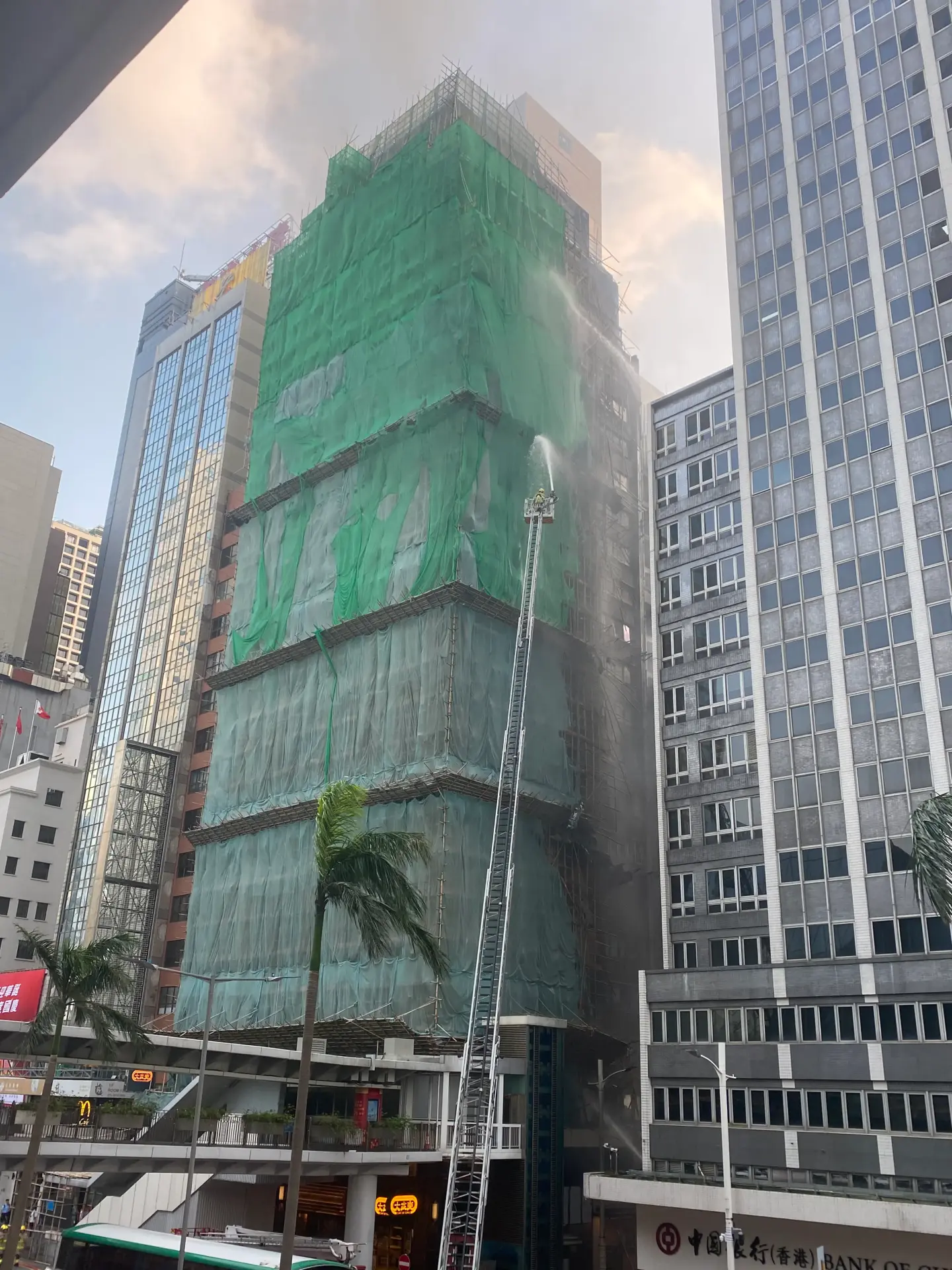 截至晚上 7 時，封路仍未解除，現場可見華懋大廈外牆被熏黑，玻璃窗破裂，部分鐵片懸吊半空，路面散落大量燃燒殘骸。(圖：網絡翻攝)