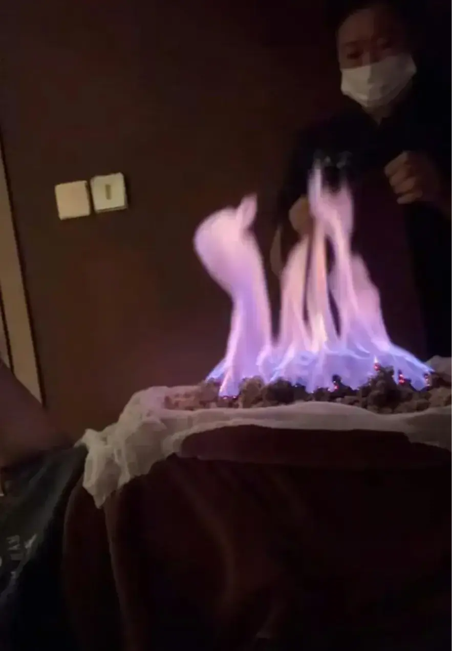 畫面中技師在其鋪了厚毛巾的肚皮上點火，烈火熊熊燃燒，視覺衝擊力極強，他卻笑言「準備燒雞翼」，淡定反應引發熱議。(圖：視頻翻攝)