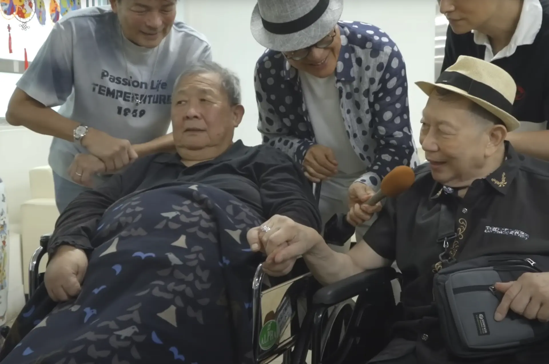 隨後一行人轉往土瓜灣探望 81 歲的秦煌，氣氛轉為歡樂。雖因心臟問題導致雙腳發黑腫脹、無法穿鞋，但秦煌精神奕奕，見到羅浩楷時雙手緊握久久不願分開。(圖： 老友鬼鬼GoodGoodBuddy@YouTube)