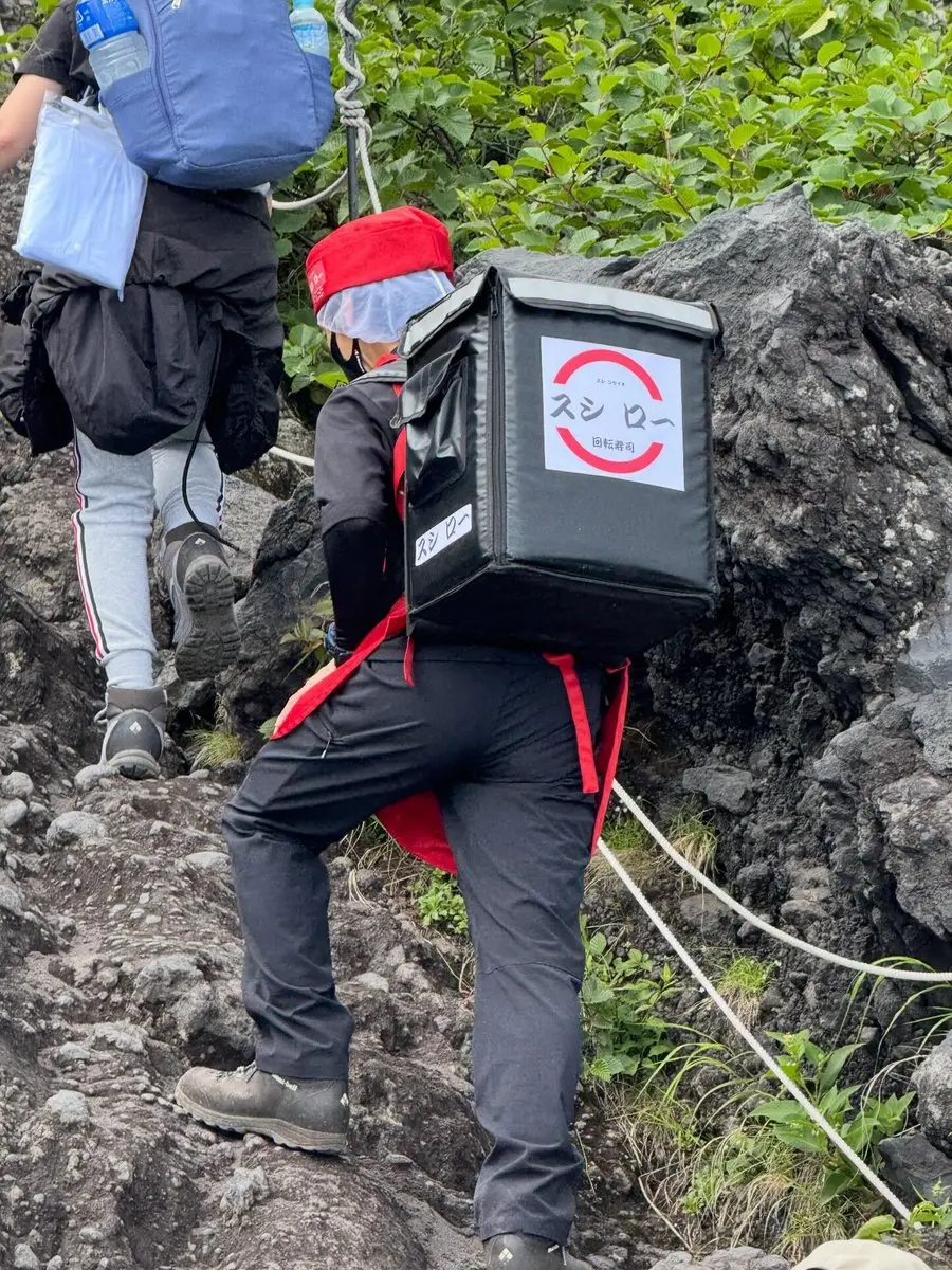中國香港女網友登富士山時，巧遇身穿壽司郎制服、攜帶餐盒登山的神秘外送員，畫面瘋傳引發各界猜測。真相揭曉，這是知名山友的趣味角色扮演，過去他還有不少驚喜造型。（來源：zxchahahaha@X）