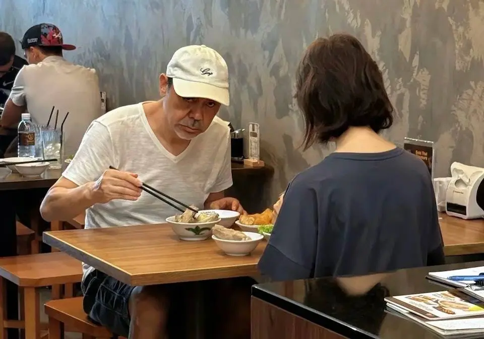 61 歲的劉青雲身著白色 T 恤、頭戴鴨舌帽，打扮隨意低調，與 58 歲的妻子郭藹明相對而坐，正在享用美食。(圖：小紅書)