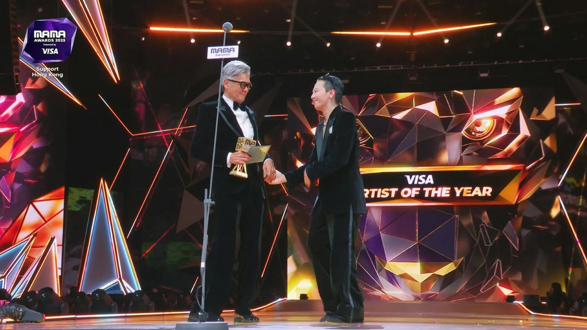 默哀結束後，周潤發才逐漸平復心情，恢復招牌的鬼馬本色：「多謝MAMA畀我這個機會，我等了七年才再上這個舞台，等到頭髮都白晒。」他更用韓語笑着催促「快啲快啲」，引出本屆大獎得主——G-Dragon（GD）。兩人台上手拖手互動，掀起全場高潮。(圖：視頻截圖)