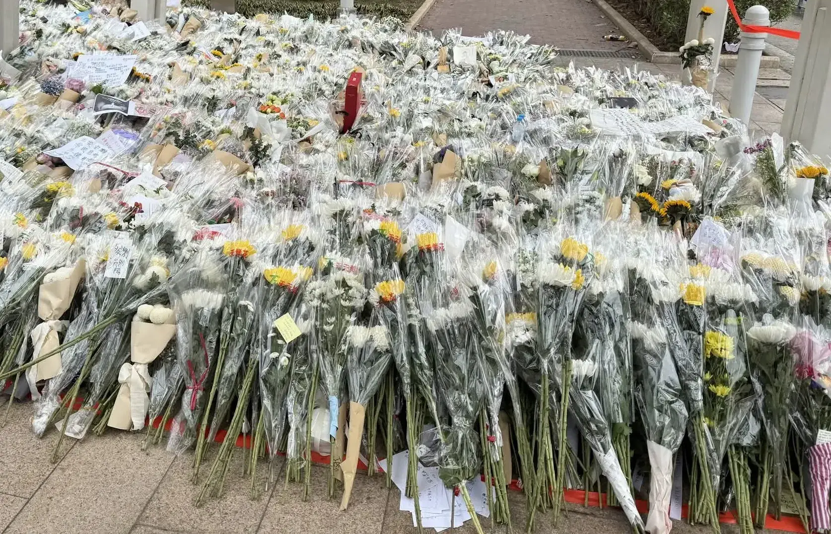 現場所見，白色菊花與黃色康乃馨漸漸堆成花海。不少市民蹲在花叢旁，細心地將手寫紙條貼在花束上，「願逝者安息」「傷者早日康復」的字樣格外醒目。有長者拄着拐杖緩步走來，放下花束後靜靜鞠躬，眼角的濕潤被午間陽光映得清晰。(圖：網絡截圖)