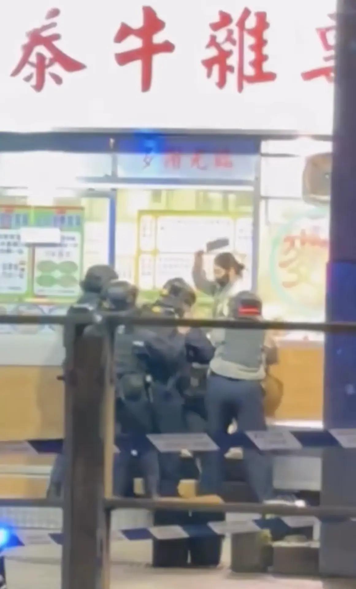 當警員嘗試開啟店門進入時，該女子情緒更為激動，持菜刀連續劈向警員盾牌，現場傳出清晰的「啪啪」撞擊聲，引發現場圍觀途人嘩聲四起。(圖：視頻截圖)