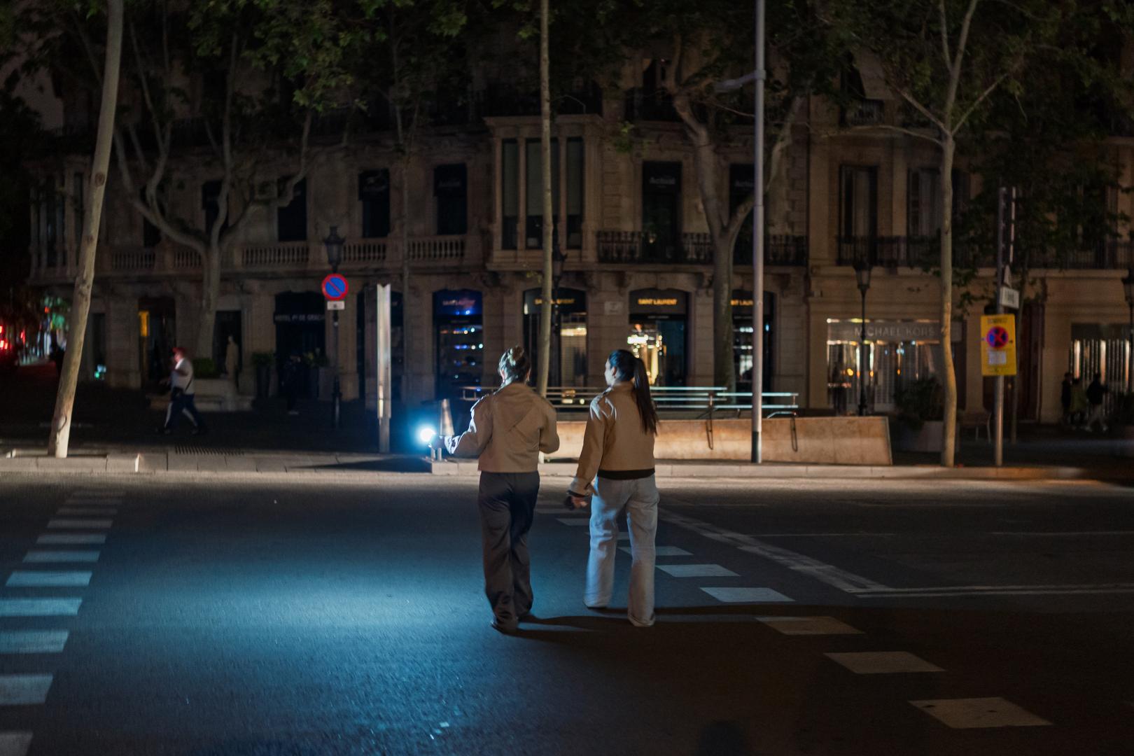 4月28日，在西班牙巴塞隆納，一名女子用手機的手電筒照明穿過人行道。（新華社）