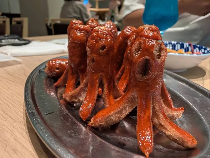 日本網友nea_vrc在社群平台X（前Twitter）分享餐廳獵奇章魚熱狗，熱狗切出猙獰五官，照片曝光吸引370萬人次瀏覽，網友瘋玩克蘇魯梗，笑稱古神降臨。（來源：nea_vrc@X）